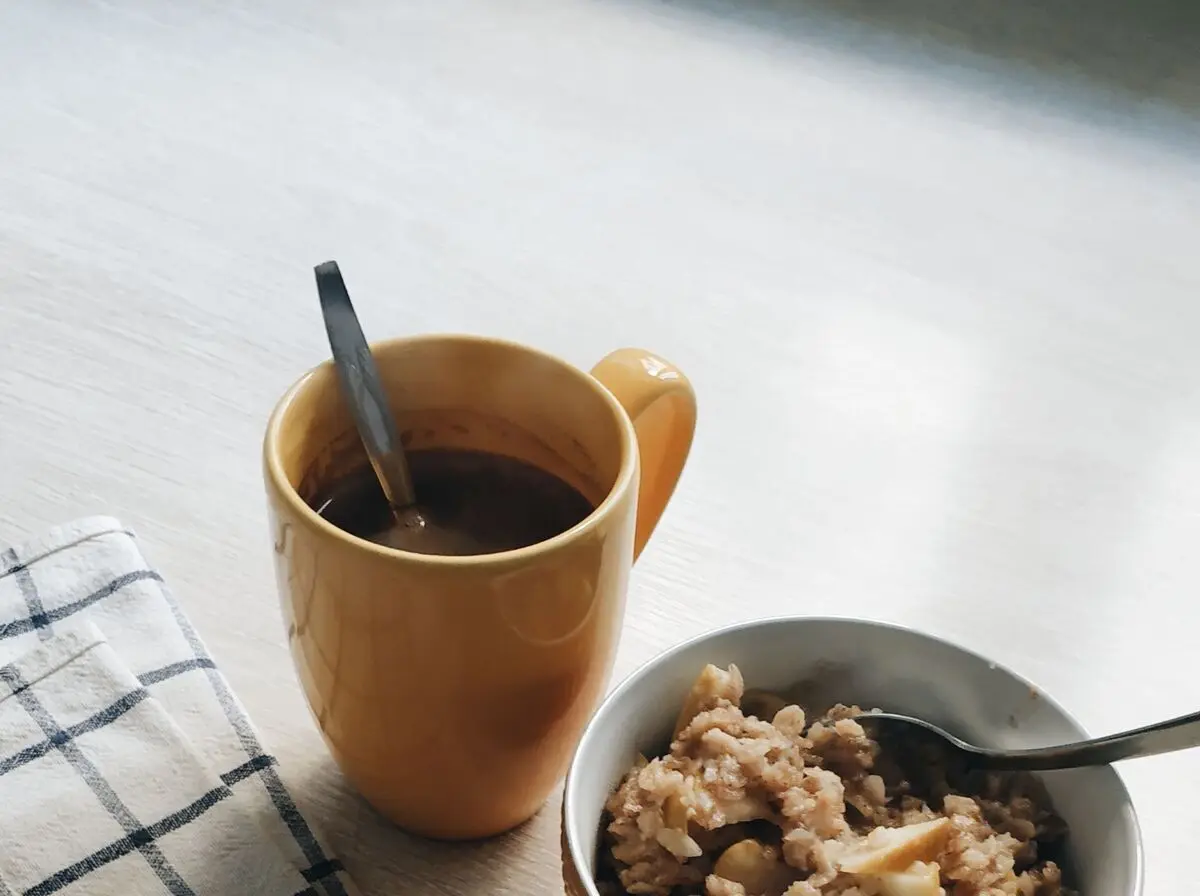 Küchentisch mit einer Schüssel Haferflocken, einem Apfel, einem Wasserglas und einem aufgeschlagenen Notizheft